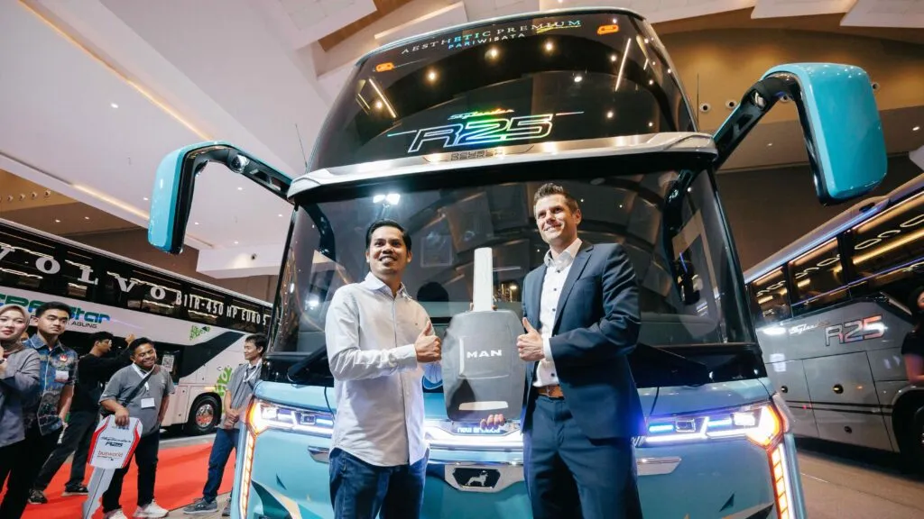Representatives from MAN and local partners celebrate with a giant decorative key in front of a turquoise New Armada double-decker bus at the Busworld Southeast Asia 2026. (Photo: MAN Truck & Bus)