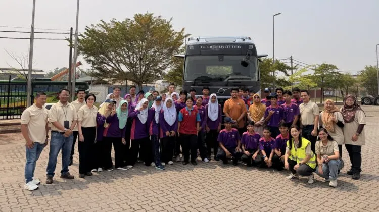 A large group of students and facilitators posing together in front of a heavy-duty Volvo Globetrotter truck outdoors at a service dealership lot.
