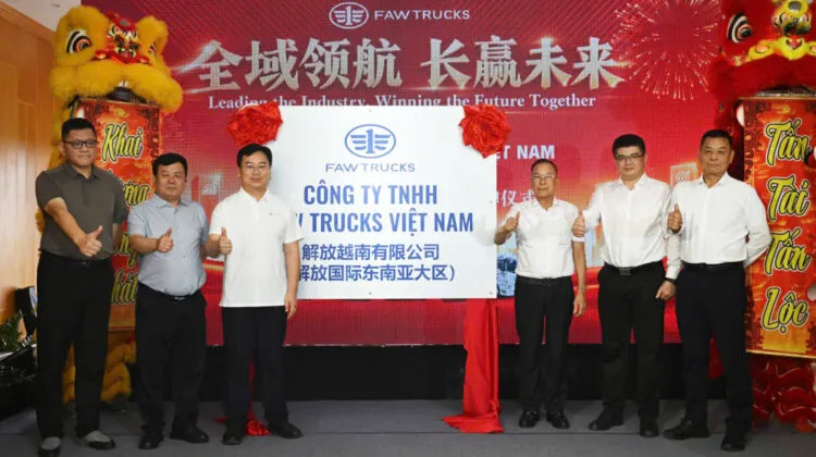 Executives giving thumbs-up gestures beside an official white plaque unveiling FAW Trucks Vietnam Co Ltd with a festive red backdrop.