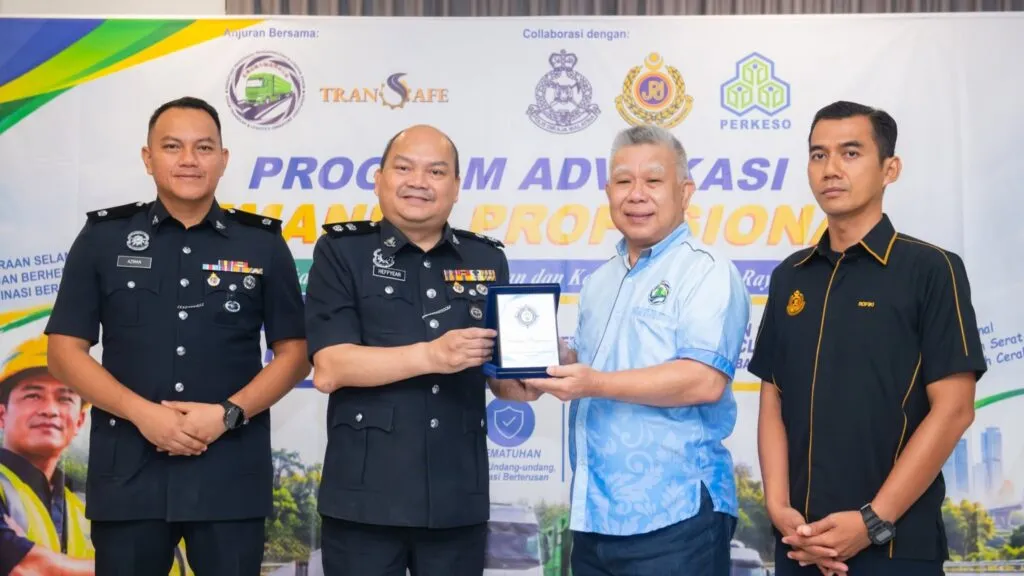 Four male officials in uniform and corporate attire posing together on stage during a souvenir presentation ceremony at the Professional Driver Advocacy Programme backdrop.