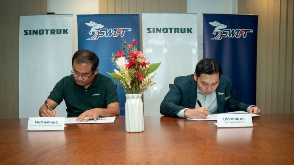 Tang Hai Yang and Loo Yong Hui seated at a wooden table signing documents in front of Sinotruk and Swift banner stands.