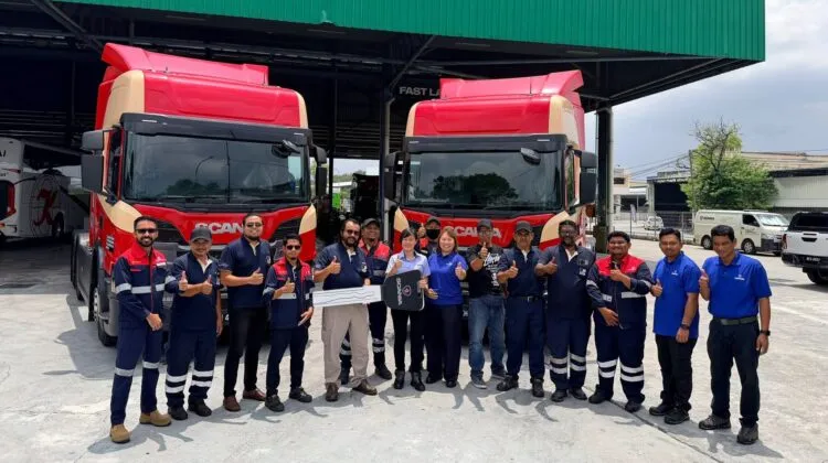 Representatives and drivers from Circular Agency and Scania Malaysia posing together with thumbs-up gestures around a giant mock key in front of two red Scania Super P460 trucks