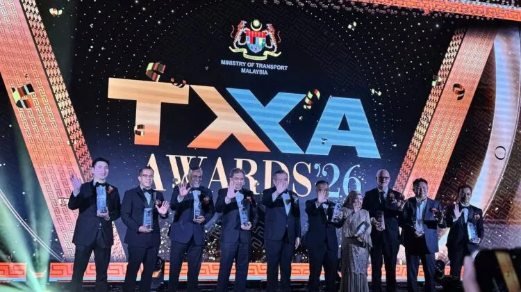 Swift Group CEO Loo Yong Hui and other corporate leaders in black tuxedos holding trophies and waving on stage under the Ministry of Transport Malaysia TXA Awards '26 digital screen.