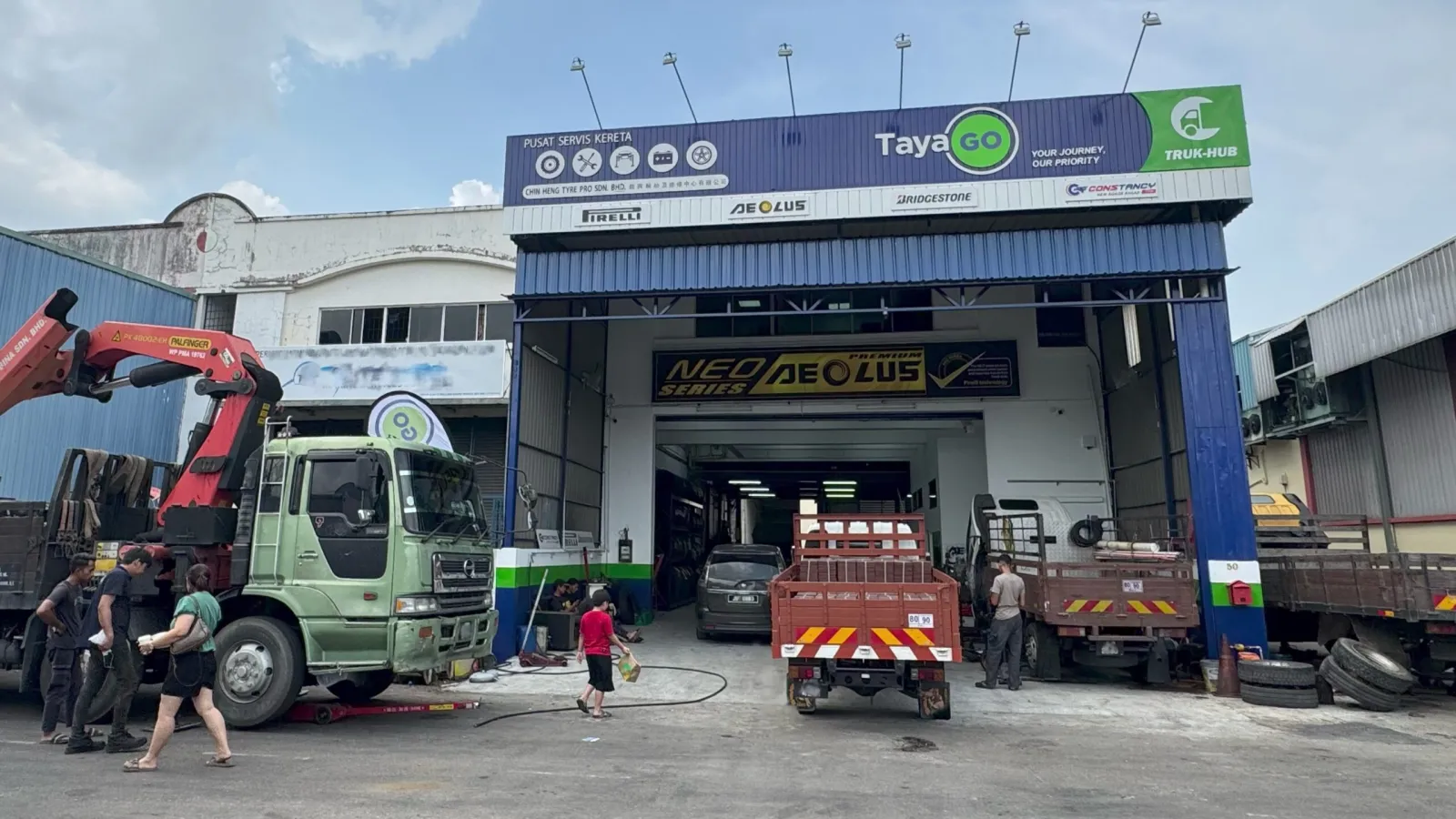 Exterior facade of Chin Heng Tyre Pro commercial truck service center under a blue Tayago Truk-Hub sign with lorries and technicians in the driveway.