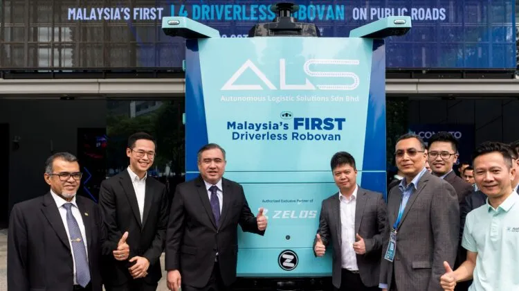 Transport Minister Anthony Loke giving a thumbs-up next to executives standing in front of a teal and white Zelostech Autonomous Logistic Solutions RoboVan.